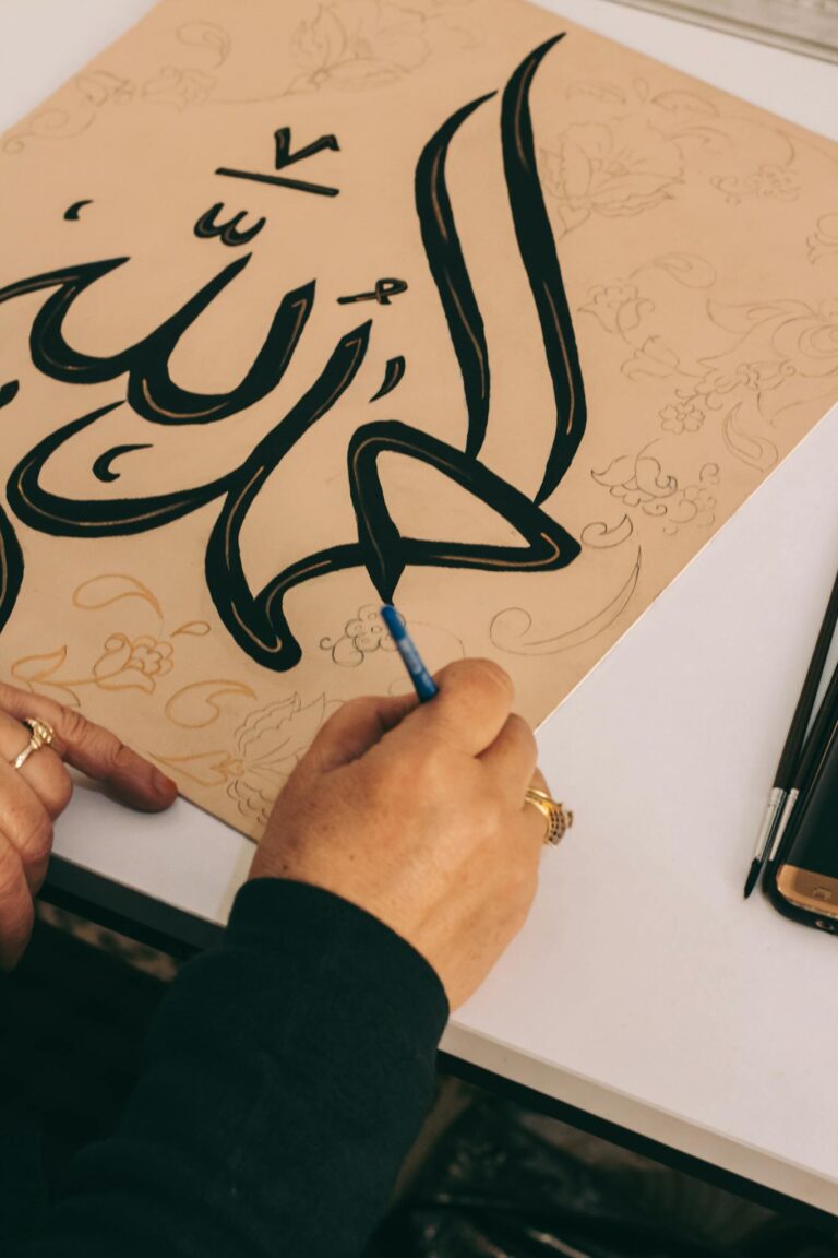 A close-up of hands creating beautiful Arabic calligraphy on paper.