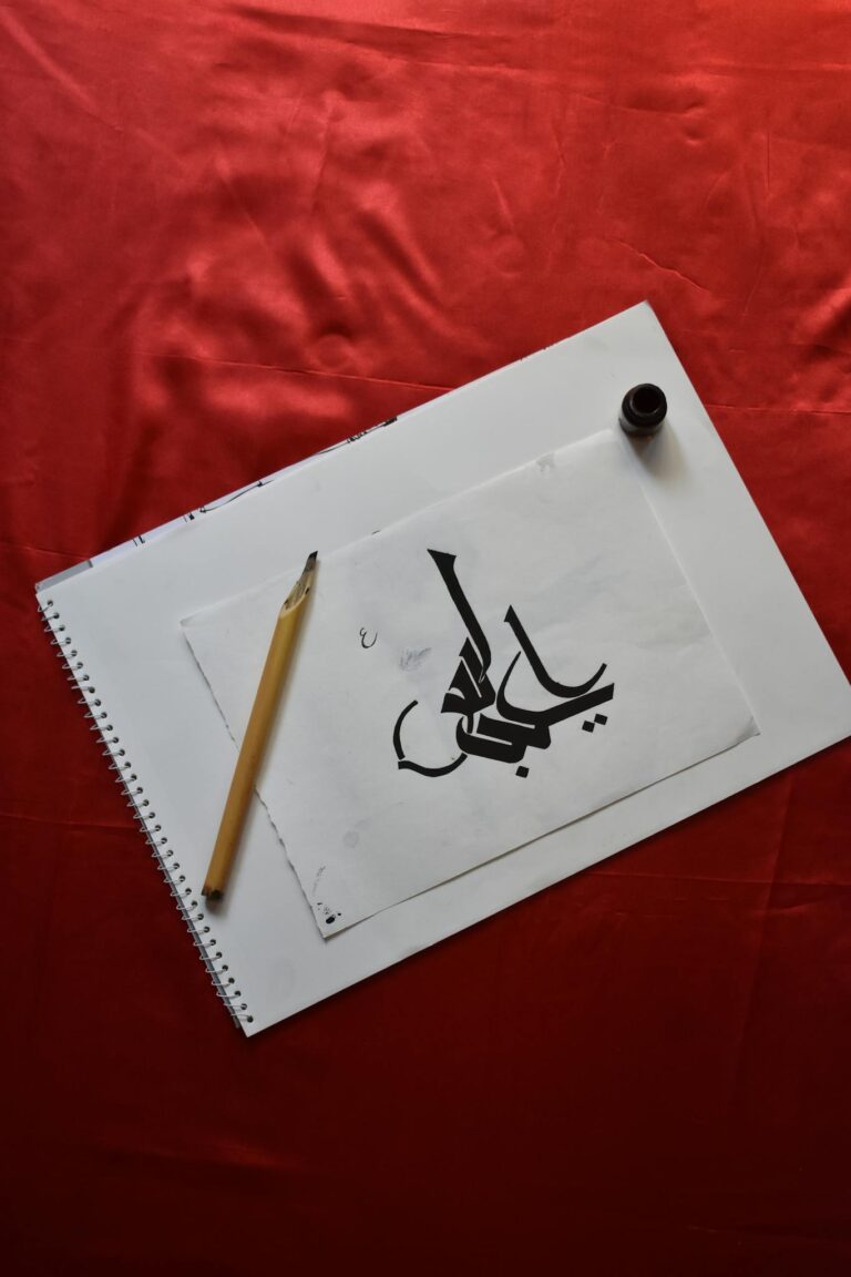 Elegant Arabic calligraphy on paper with a pencil and ink on a red background, showcasing traditional art.